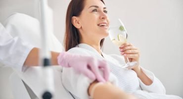 Joyous female patient drinking a healthy beverage during a medical procedure in a beauty clinic